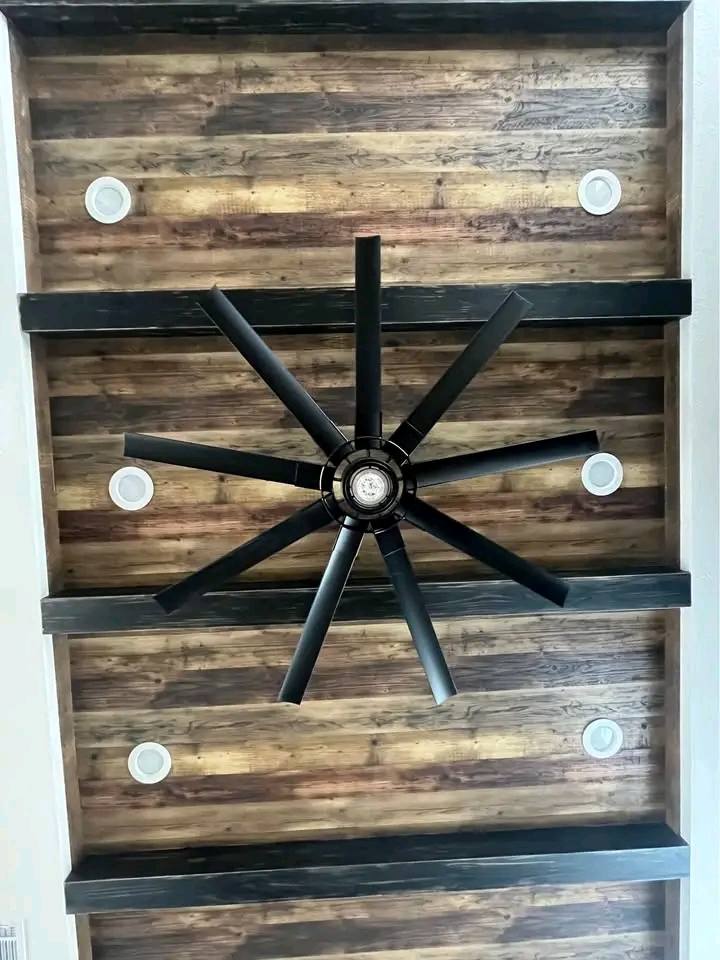 Ceiling with rustic wooden panels, featuring a large black fan at the center. Four round ceiling lights are symmetrically placed, creating a modern, cozy atmosphere.