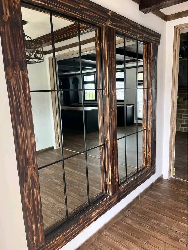 A rustic interior with large wooden-framed mirrors reflecting a room with wooden floors. The atmosphere is warm, with natural light and a cozy tone.