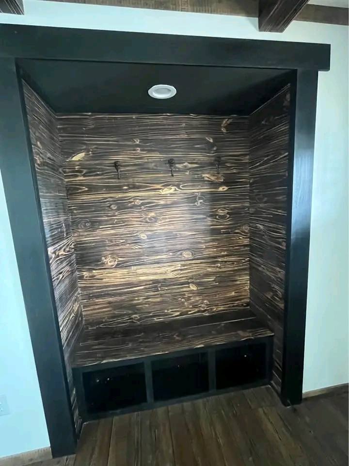 Cozy wooden alcove with rustic paneling, featuring two hooks on the back wall and a bench with cubby storage underneath, set under soft lighting.