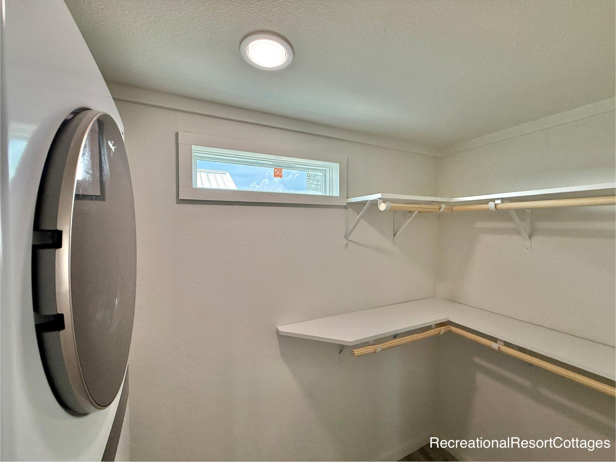 Bright laundry room with a modern washer on the left, a small rectangular window above, and an L-shaped white countertop with wooden shelves on the right.