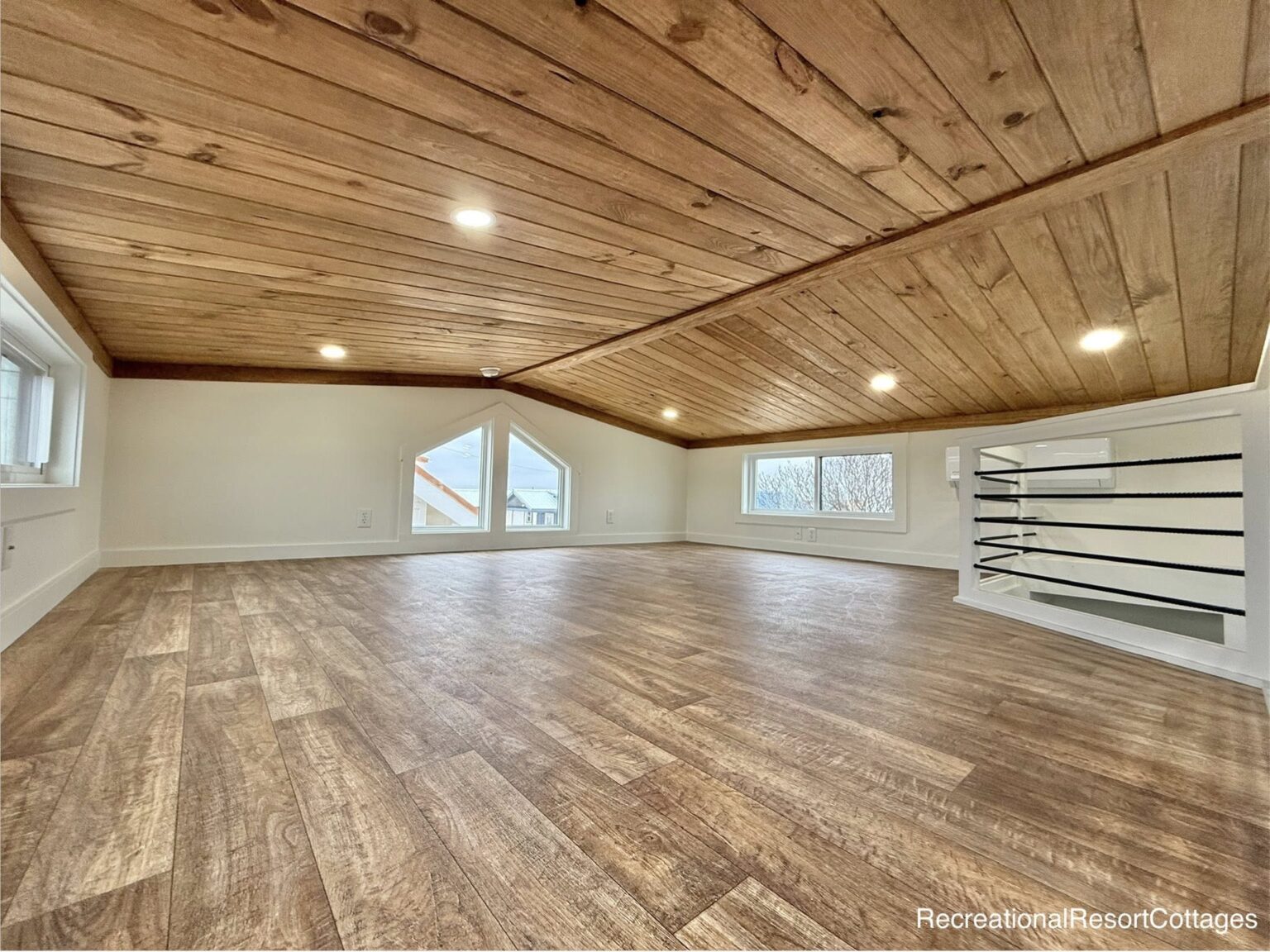 Spacious attic with wooden floor and ceiling, featuring recessed lighting and large windows at each end. Bright, cozy, and rustic atmosphere.