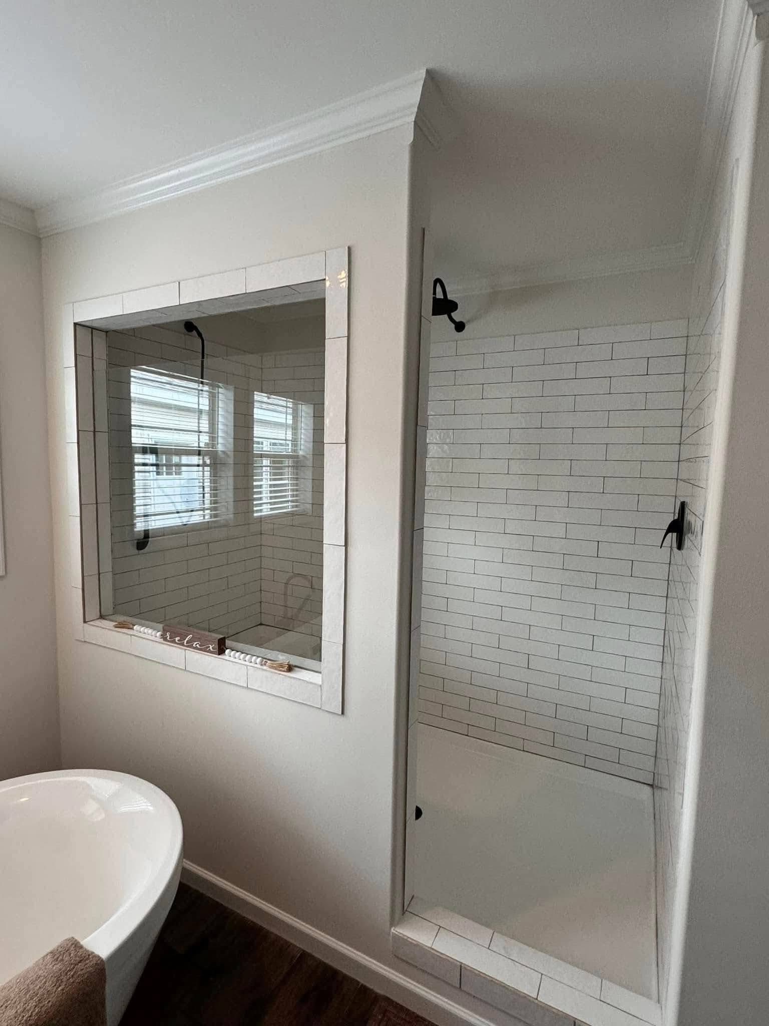 Modern bathroom with white subway tiles, featuring a walk-in shower and a freestanding tub. A window offers natural light. Calm, clean ambiance.