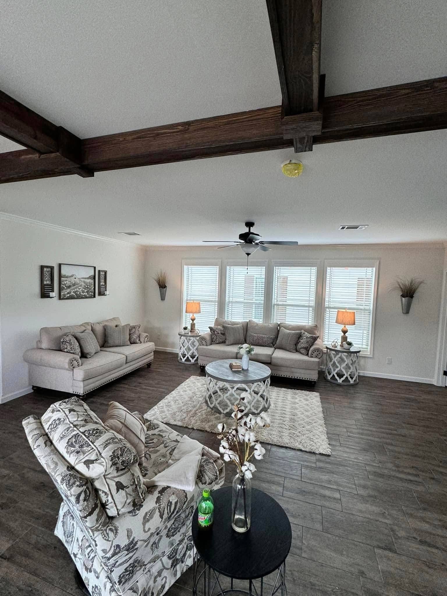 Spacious living room with floral-patterned chairs, two beige sofas, round coffee table on a shag rug, table lamps, and large windows letting in natural light.