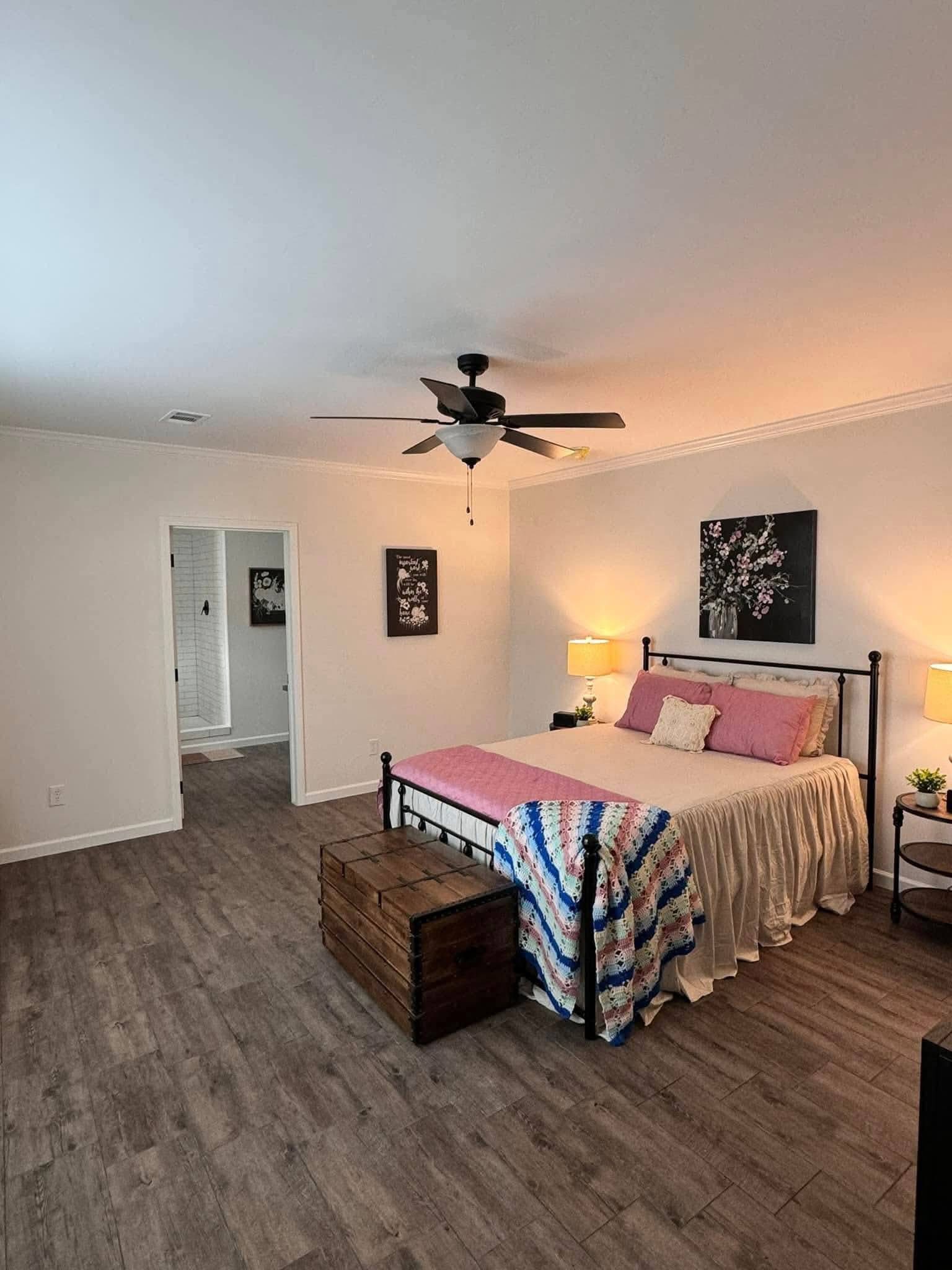 Cozy bedroom with a double bed featuring pink and white bedding and a crochet blanket. A wooden chest and bedside tables with lamps add warmth.