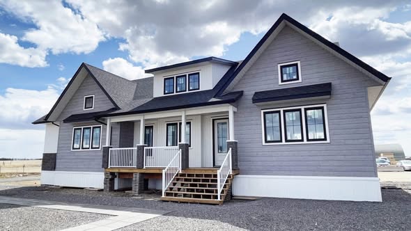 Two-story modern gray house with white trim, black roof, and a wooden porch. Set against a cloudy sky, conveying a serene suburban feel.