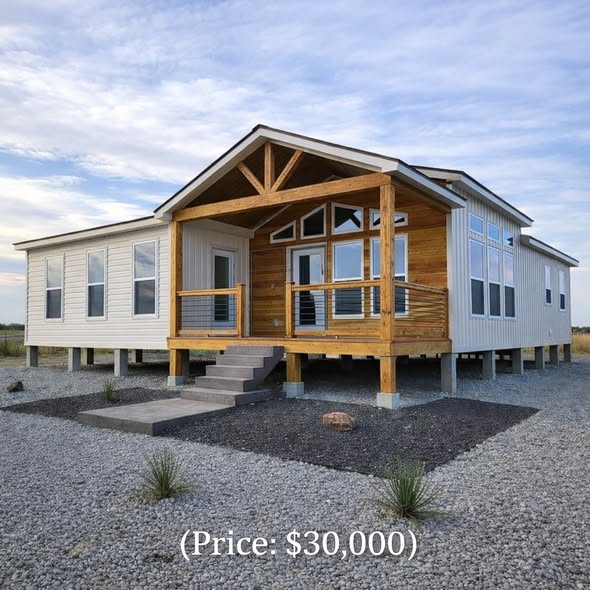 Modern prefab home with a wooden porch and large windows, set on a gravel lot under a blue sky. The price shown is $30,000.